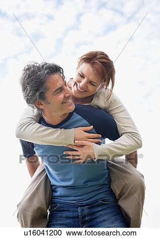 Stock Image - Man giving woman a piggy back ride. Fotosearch