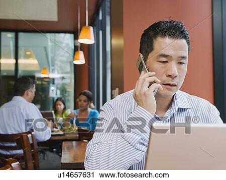 Stock Image - Man talking on phone and working on laptop in restaurant. Fotosearch