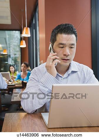 Stock Photograph - Man talking on phone and working on laptop in restaurant. Fotosearch