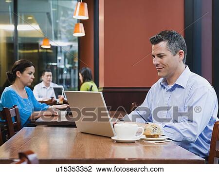 Stock Image - Man working on laptop in restaurant. Fotosearch