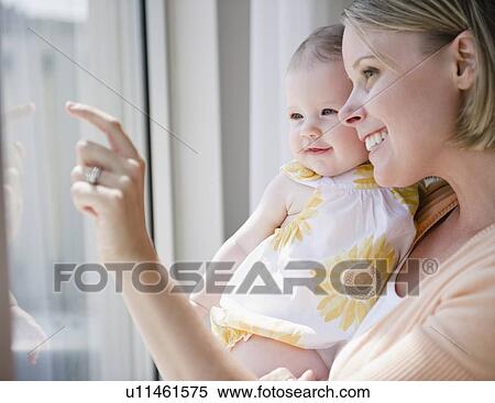 Stock Photography - Mother and baby daughter looking out window. Fotosearch