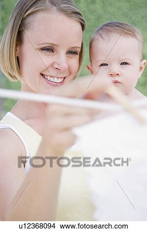 Picture - Mother holding baby while hanging up the laundry. Fotosearch