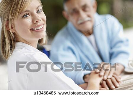 Stock Photography - Nurse and senior man holding hands. Fotosearch