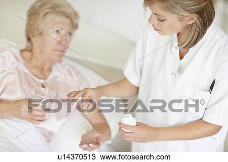 Stock Image - Nurse giving pill to senior woman. Fotosearch