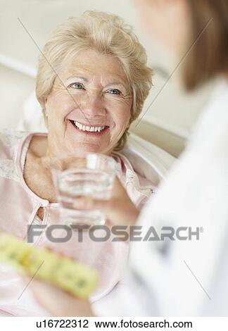 Stock Image - Nurse giving pill to senior woman. Fotosearch
