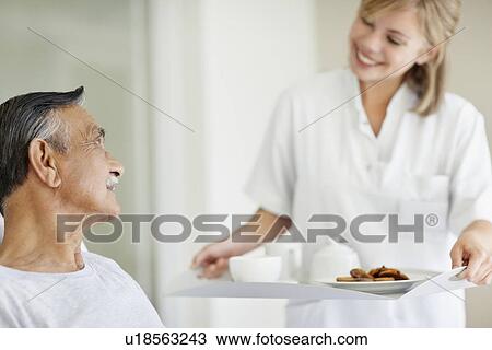 Stock Image - Nurse giving tray of food to patient. Fotosearch