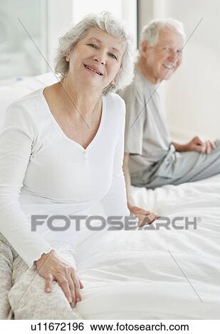 Stock Photograph - Relaxed senior couple sitting on bed. Fotosearch