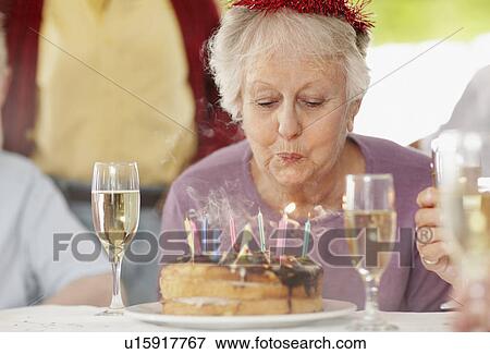 Senior woman blowing out the candles on a birthday cake View Large Photo Image Stock Photo - Senior woman blowing out the candles on a birthday cake. Fotosearch