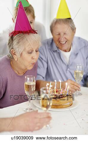 Senior woman blowing out the candles on a birthday cake View Large Photo Image Stock Photo - Senior woman blowing out the candles on a birthday cake. Fotosearch