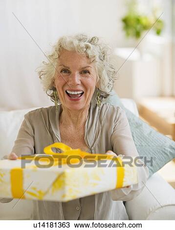 Stock Image - Surprised woman receiving a birthday gift. Fotosearch