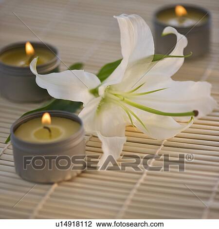Stock Image - Tea lights and white lily on bamboo mat. Fotosearch