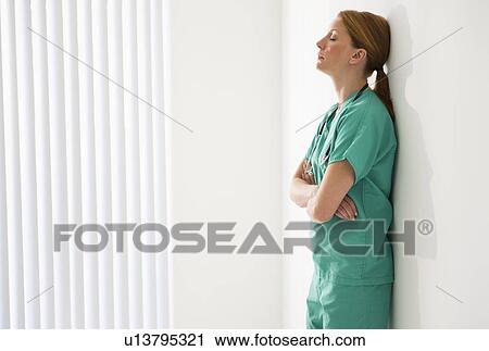 Stock Image - Tired doctor leaning against wall. Fotosearch