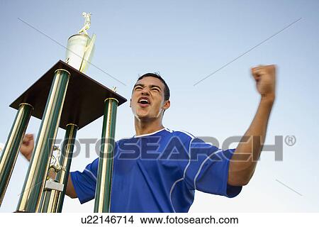 Trophy in front of cheering soccer player View Large Photo Image Picture - Trophy in front of cheering soccer player. Fotosearch