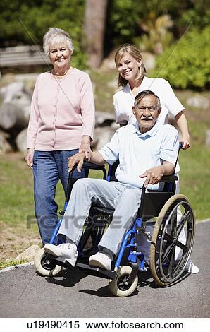 Stock Photography - Two women walking with man in a wheelchair. Fotosearch