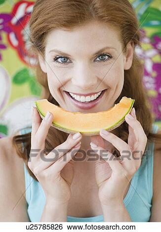 Stock Photograph - Woman eating a slice on cantaloupe. Fotosearch