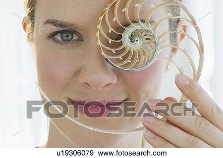 Stock Photo - Woman holding a nautilus shell in front of her eye. Fotosearch