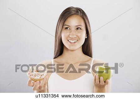 Woman holding an doughnut and an apple View Large Photo Image Picture - Woman holding an doughnut and an apple. Fotosearch