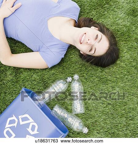 Woman lying on grass beside recycling bin View Large Photo Image Stock Image - Woman lying on grass beside recycling bin. Fotosearch