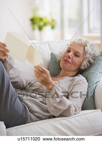 Stock Image - Woman reading mail while relaxing on couch. Fotosearch