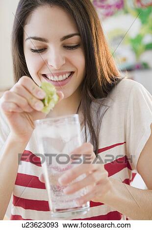 Stock Image - Woman squeezing lime into water. Fotosearch