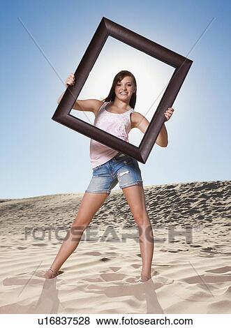 Stock Photo - Woman standing on beach holding picture frame. Fotosearch