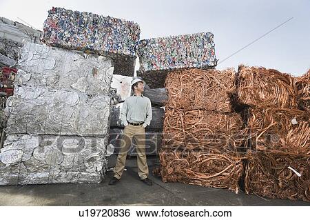 Worker standing beside stacks of recycled material View Large Photo Image Stock Photograph - Worker standing beside stacks of recycled material. Fotosearch