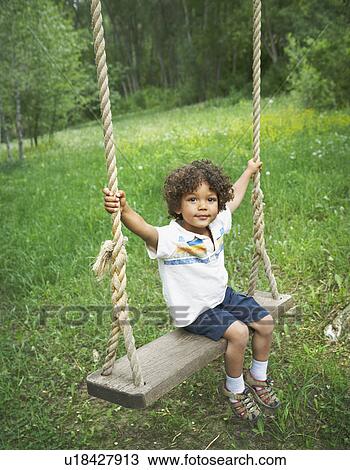 Stock Image - Young child sitting on large outdoor swing. Fotosearch