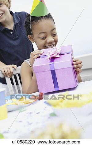 Stock Image - Young girl opening a birthday gift. Fotosearch