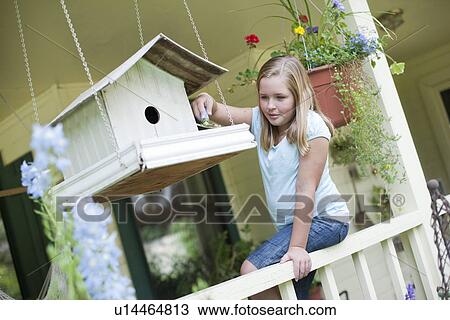 Stock Image - Young girl putting seeds in birdhouse. Fotosearch