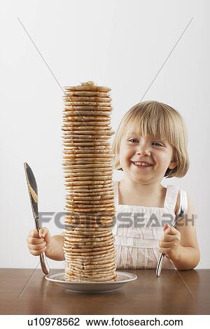 Stock Image - Young girl sitting behind a tall stack of pancakes. Fotosearch