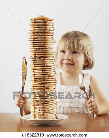 Stock Image - Young girl sitting behind a tall stack of pancakes. Fotosearch