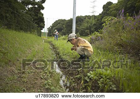 Boy crouching and looking at ditch View Large Photo Image Stock Image - Boy crouching and looking at ditch. Fotosearch