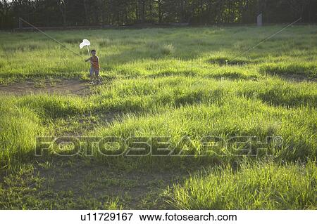 Stock Photo - Boy holding butterfly net walking in field. Fotosearch