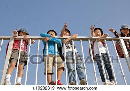 Stock Photo - Boys and girls giving thumbs up and peace sign, Low angle view, Japan. Fotosearch