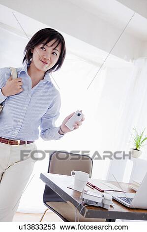 Stock Image - Businesswoman Leaving her Desk and Holding Mobile Phone. Fotosearch