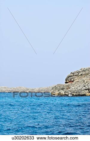 Stock Image - Clear Sky Over Rocky Coastline. Fotosearch