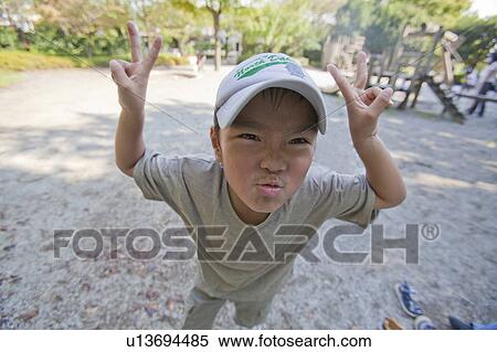 Stock Photography - Close-up of a boy making a face and peace sign, Japan. Fotosearch