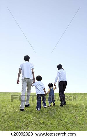 Stock Image - Family with Two Children Walking on Green Field, Holding Hands. Fotosearch