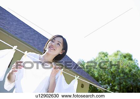 Stock Image - Mid Adult Woman Hanging Clothes. Fotosearch