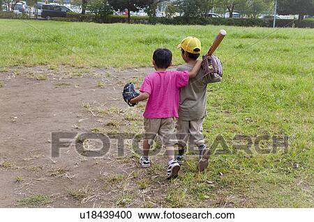 Stock Image - Rear view of boys holding baseball equipments, Japan. Fotosearch