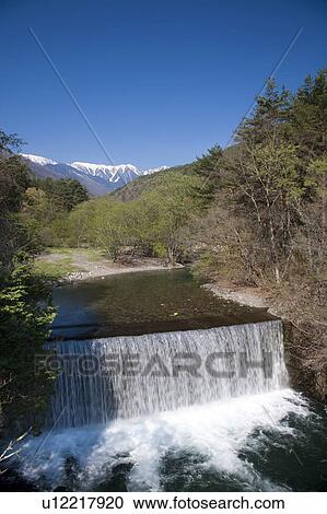 Stock Image - River Running in the Forest and Snowcapped Mountains in the Background. Fotosearch