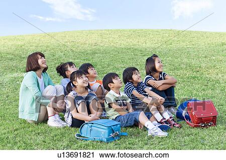 School children and female teacher sitting in field, looking away View Large Photo Image Stock Image - School children and female teacher sitting in field, looking away. Fotosearch