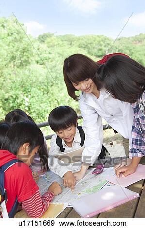 Stock Photo - School children and female teacher looking at map in park. Fotosearch