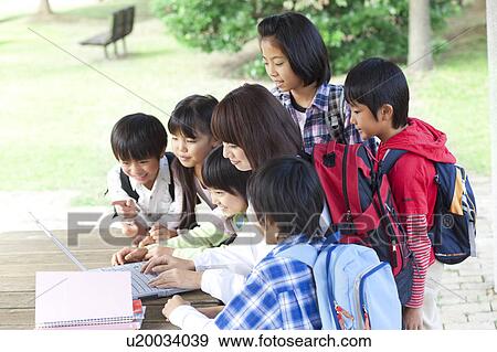 School children and female teacher using laptop in park View Large Photo Image Stock Photo - School children and female teacher using laptop in park. Fotosearch