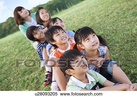 Stock Photography - School children and female teacher sitting in field, looking away. Fotosearch