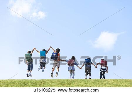 Stock Photography - School children jumping at riverbank, hand in hand, copy space. Fotosearch