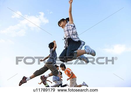 Stock Photo - School children jumping under sky, copy space. Fotosearch