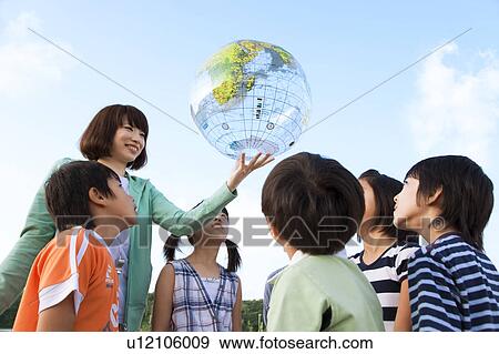 Stock Photo - School children looking at globe female teacher holding. Fotosearch