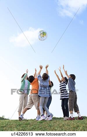 Stock Image - School children with female teacher playing with globe. Fotosearch