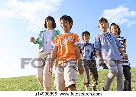 Stock Photography - School children with female teacher walking at riverbank, smiling. Fotosearch
